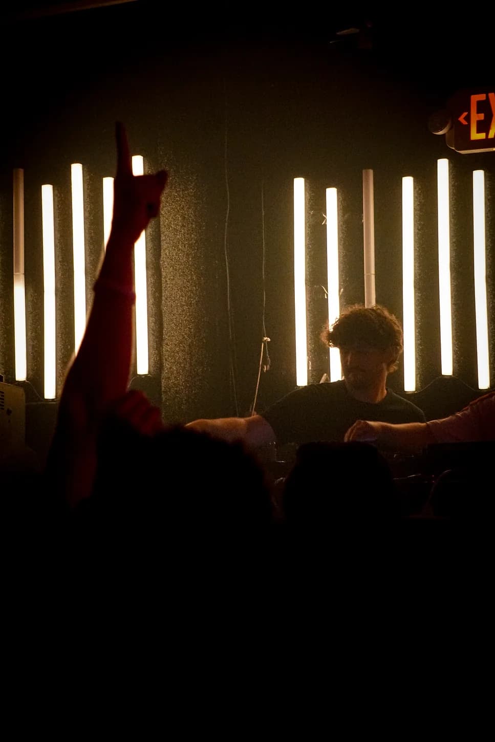 DJ performing under warm stage lighting as a hand shoots up from the crowd
